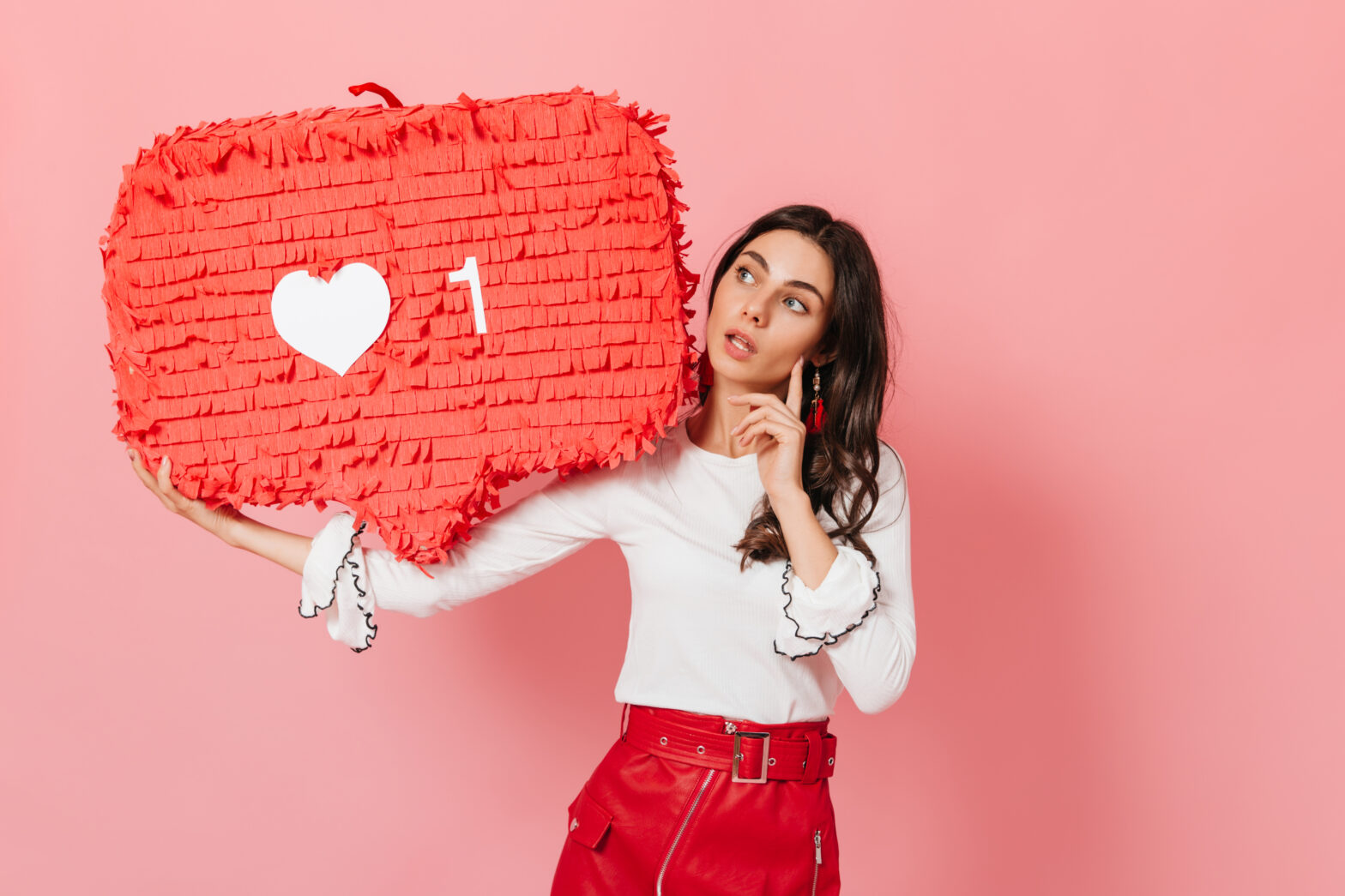 Long-haired brunette thoughtfully looks at huge red like from Instagram. Close-up shot of cute tanned girl