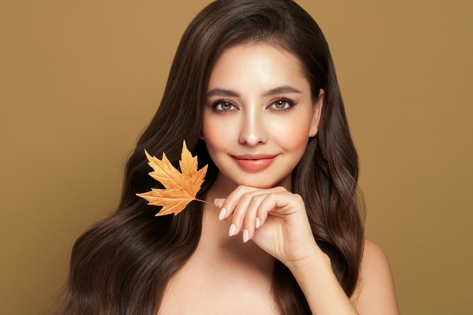 Portrait of beautiful young woman with autumn leafs. Healthy clean fresh skin natural make up.Long curly hairstyle. Care and beauty hair products.